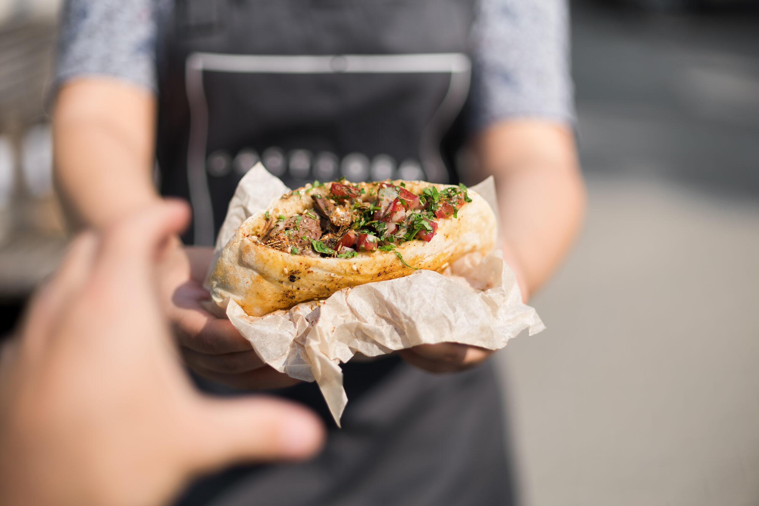 A person serving a falafel pita wrap to another person